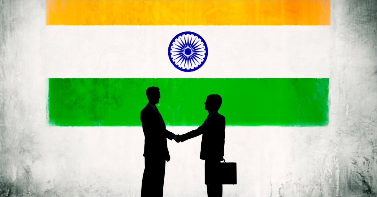 Black silhouettes of two people shaking hands in front of an India flag